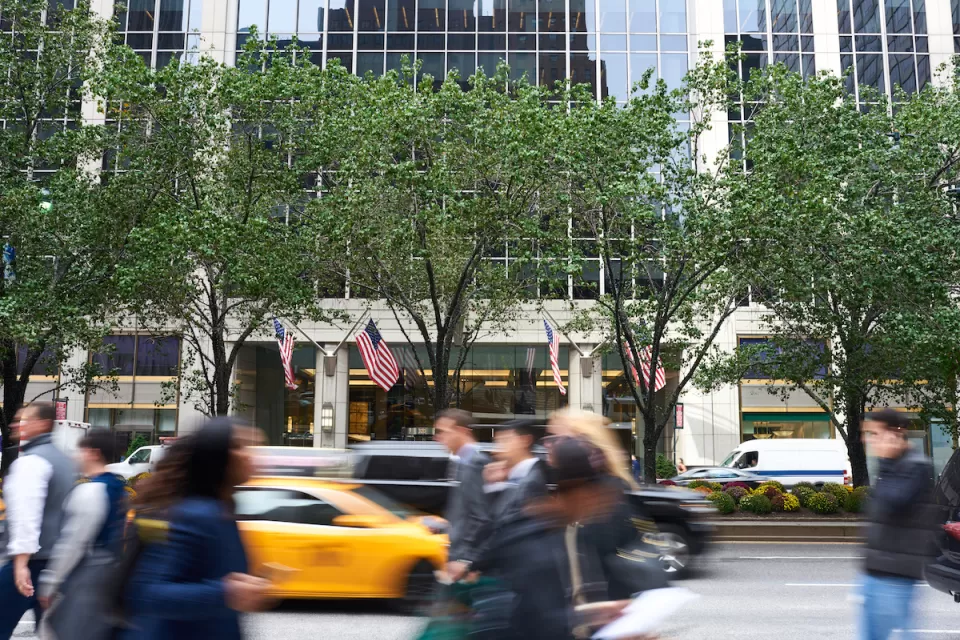 Blurred pedestrians walkingon NYC sidewalk with blurred yellow cab in background.